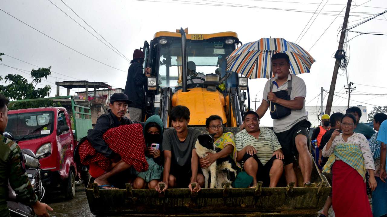 Flood-affected people sit in the scoop of a digger as they are moved to safer places during rains in Imphal East