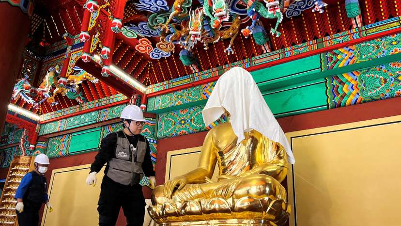Officials wraps a Buddha statue with a fire-retardant blanket to protect it from a wildfire, at Gounsa temple in Uiseong