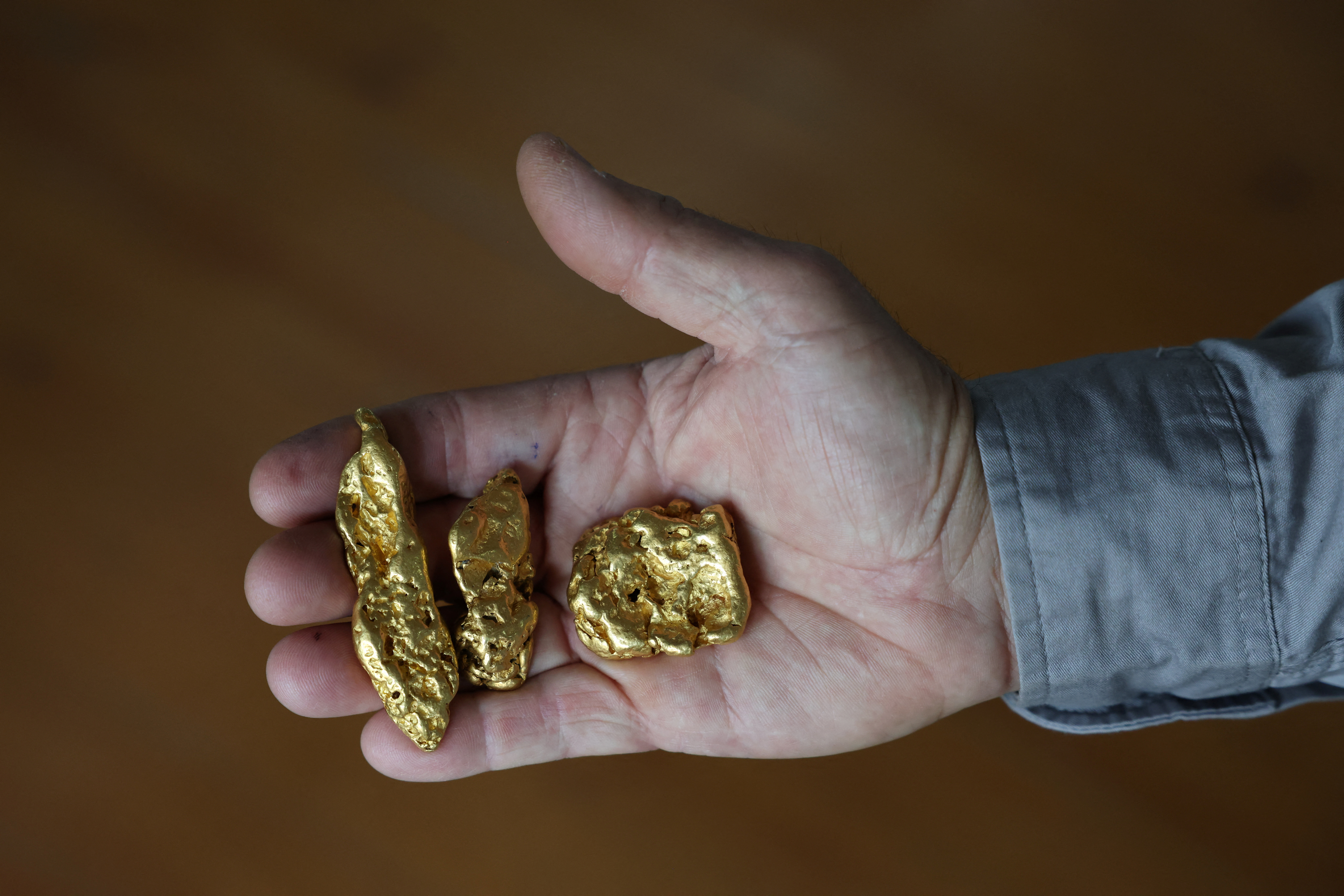 A shop worker poses holding three gold nuggets at The Gold Centre store, in Maryborough