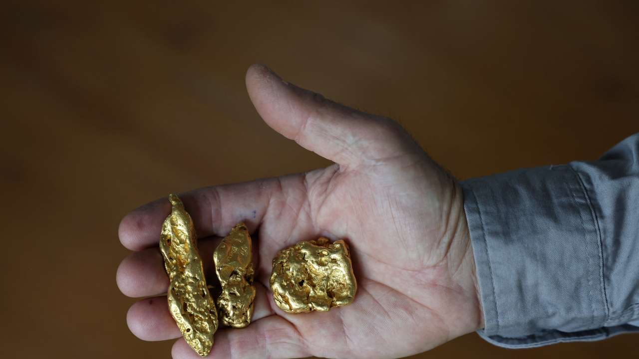 A shop worker poses holding three gold nuggets at The Gold Centre store, in Maryborough