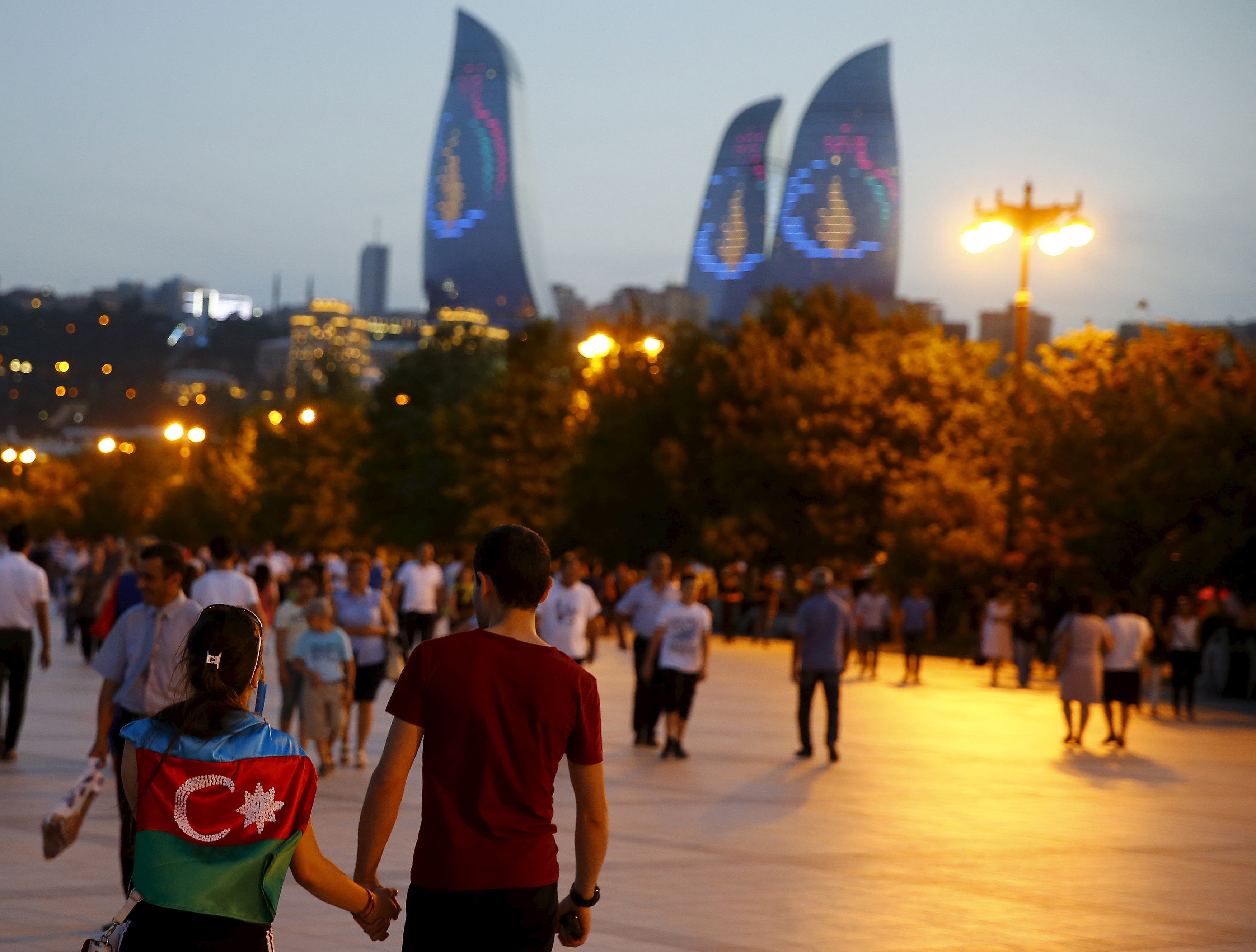A girl, draped in Azerbaijan's national flag, walks with a boy on a street in downtown Baku