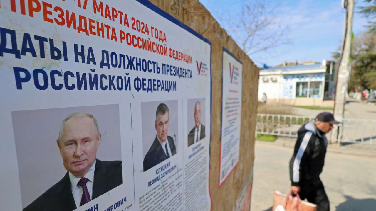 A man walks past an information board with portraits of Russian presidential candidates in the upcoming election in Yevpatoriya