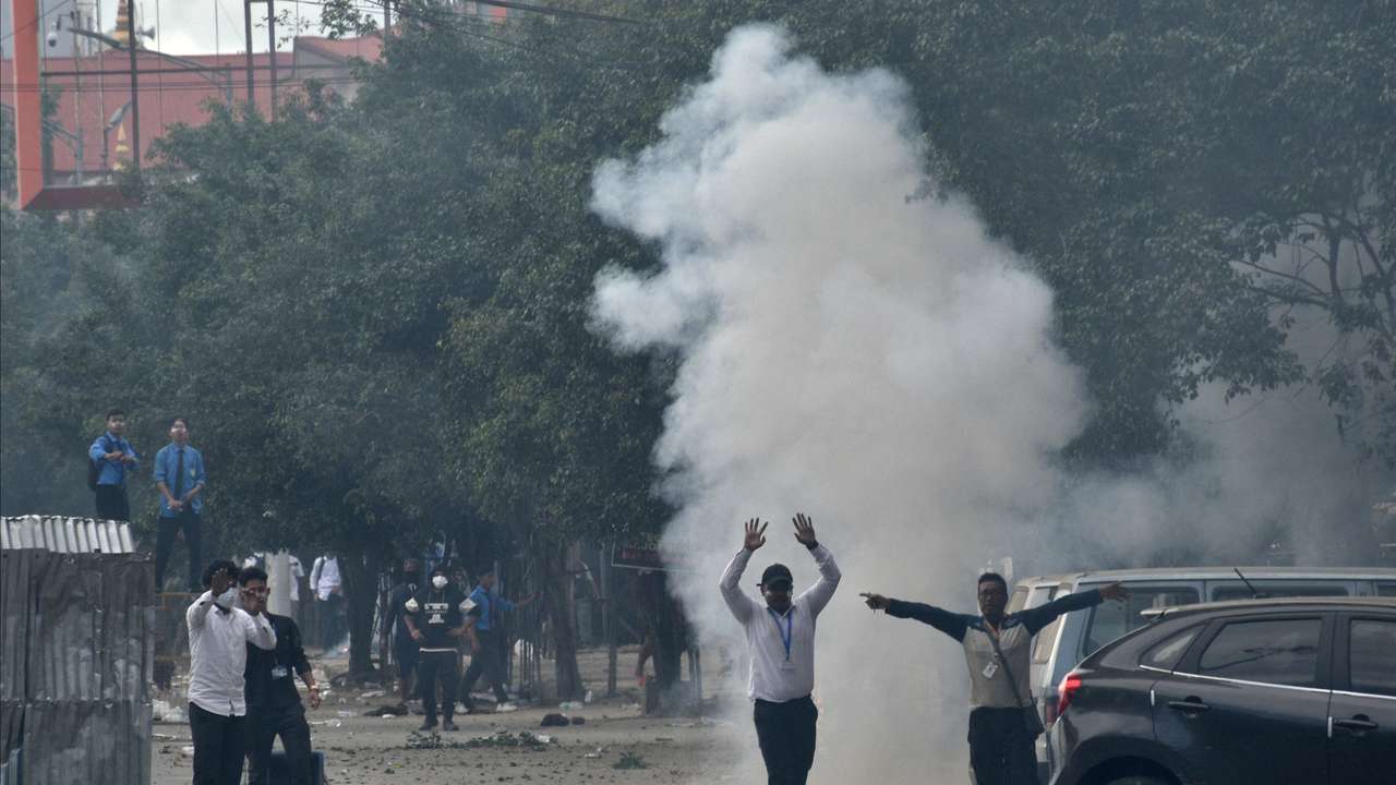 Demonstrators react as smoke billows from a tear gas shell fired by police to disperse the protesters, in Imphal