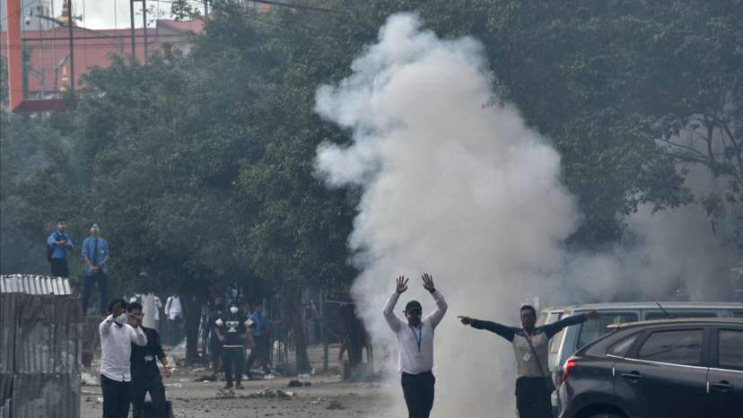 Demonstrators react as smoke billows from a tear gas shell fired by police to disperse the protesters, in Imphal