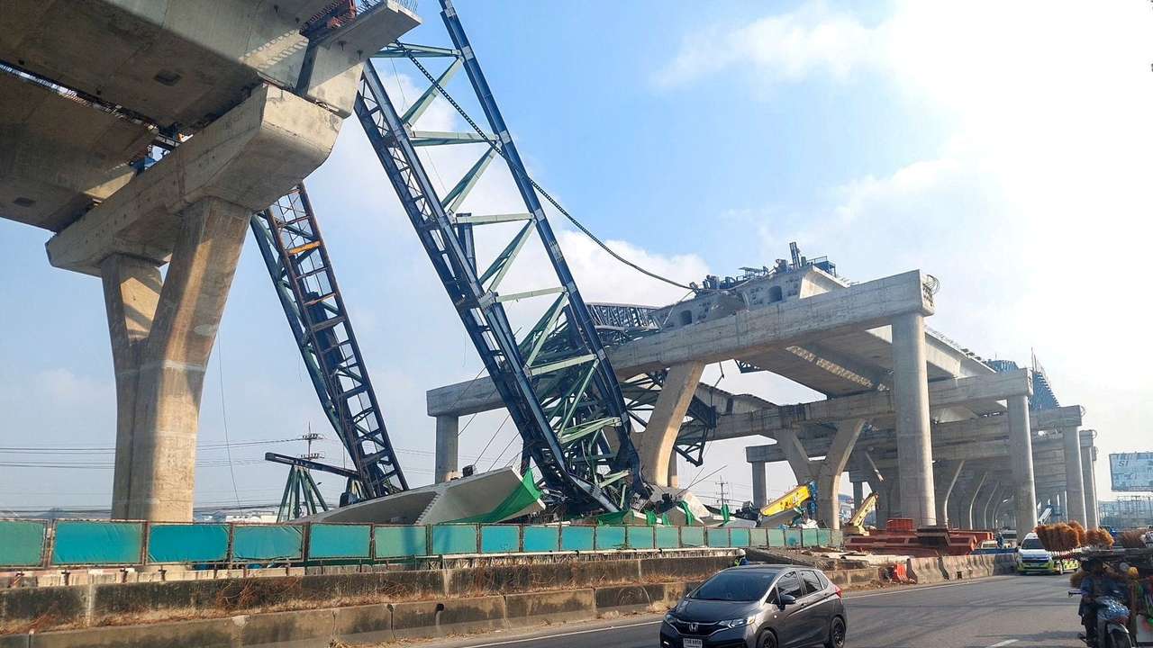 Cars drive next to a collapsed crane that crushed two vehicles during construction of an elevated highway in Samut Sakhon province