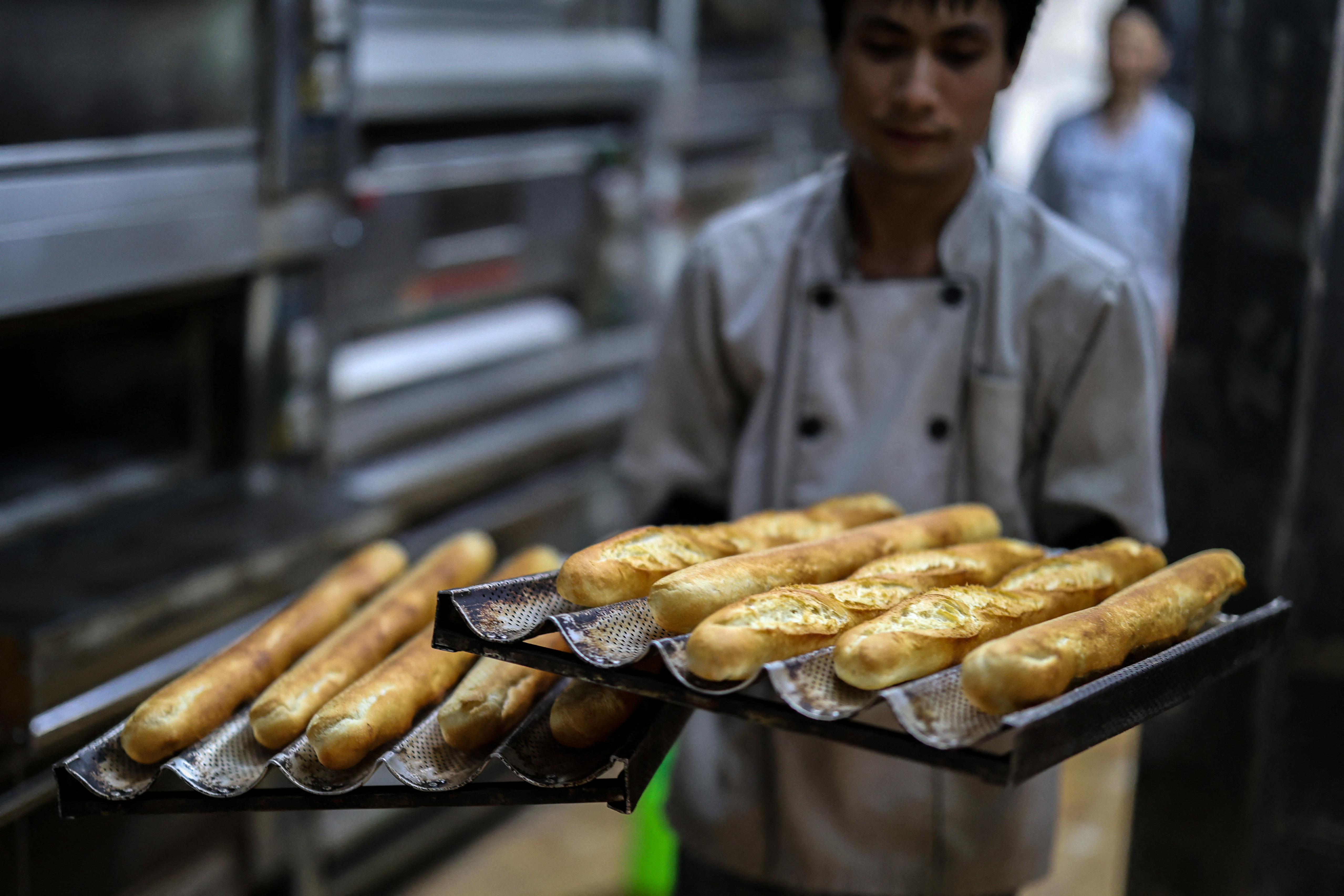 A baker holds up trays of baguettes at the Hoan Boulangerie bakery shop in Hanoi