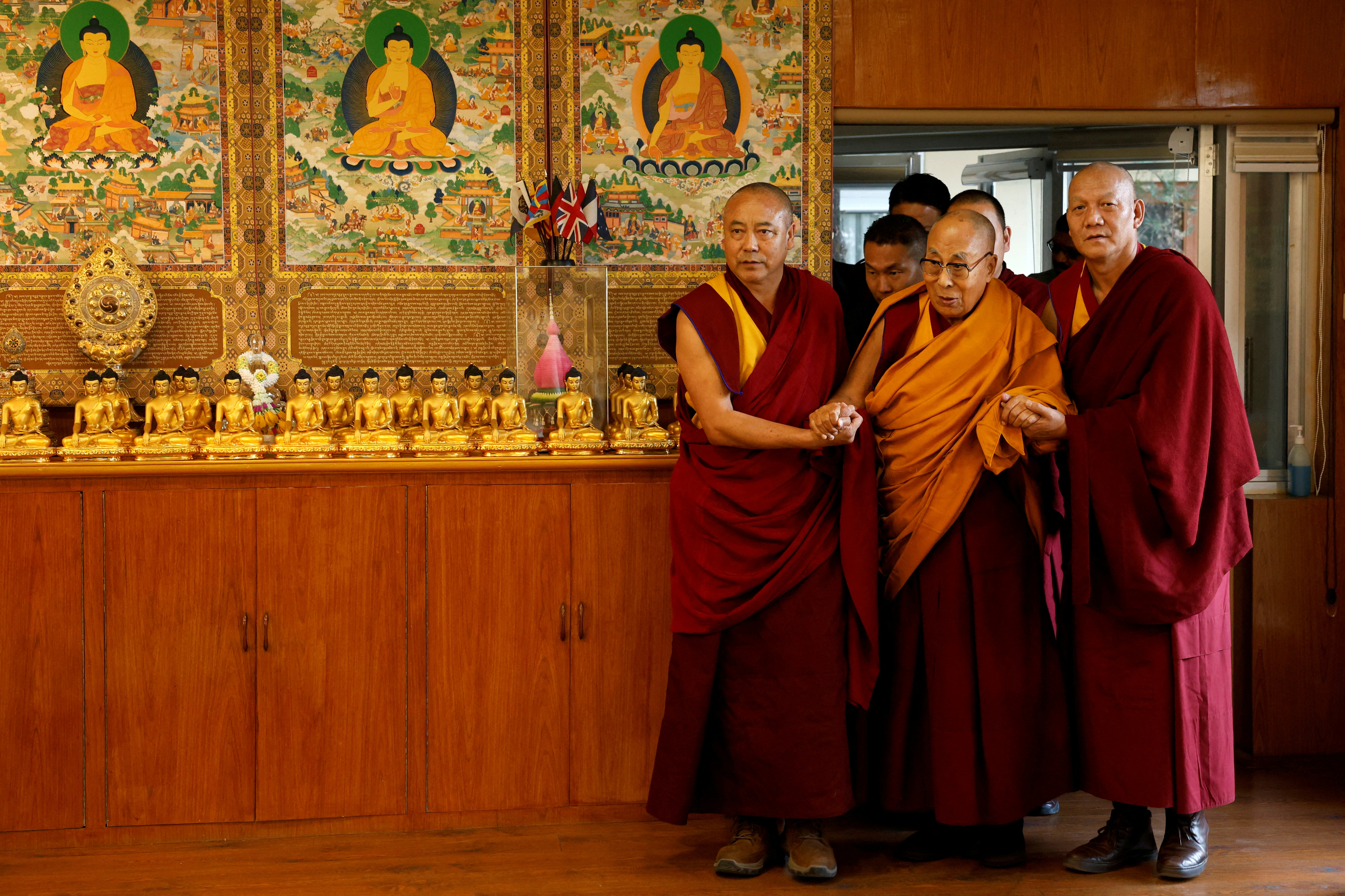 Tibetan spiritual leader, the Dalai Lama, is escorted into a hall by red-robed monks holding his hands at his Himalayan residence in Dharamshala