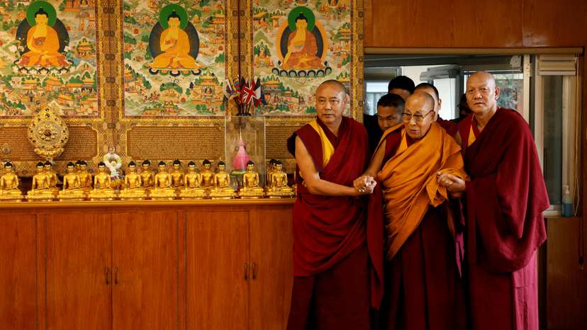 Tibetan spiritual leader, the Dalai Lama, is escorted into a hall by red-robed monks holding his hands at his Himalayan residence in Dharamshala