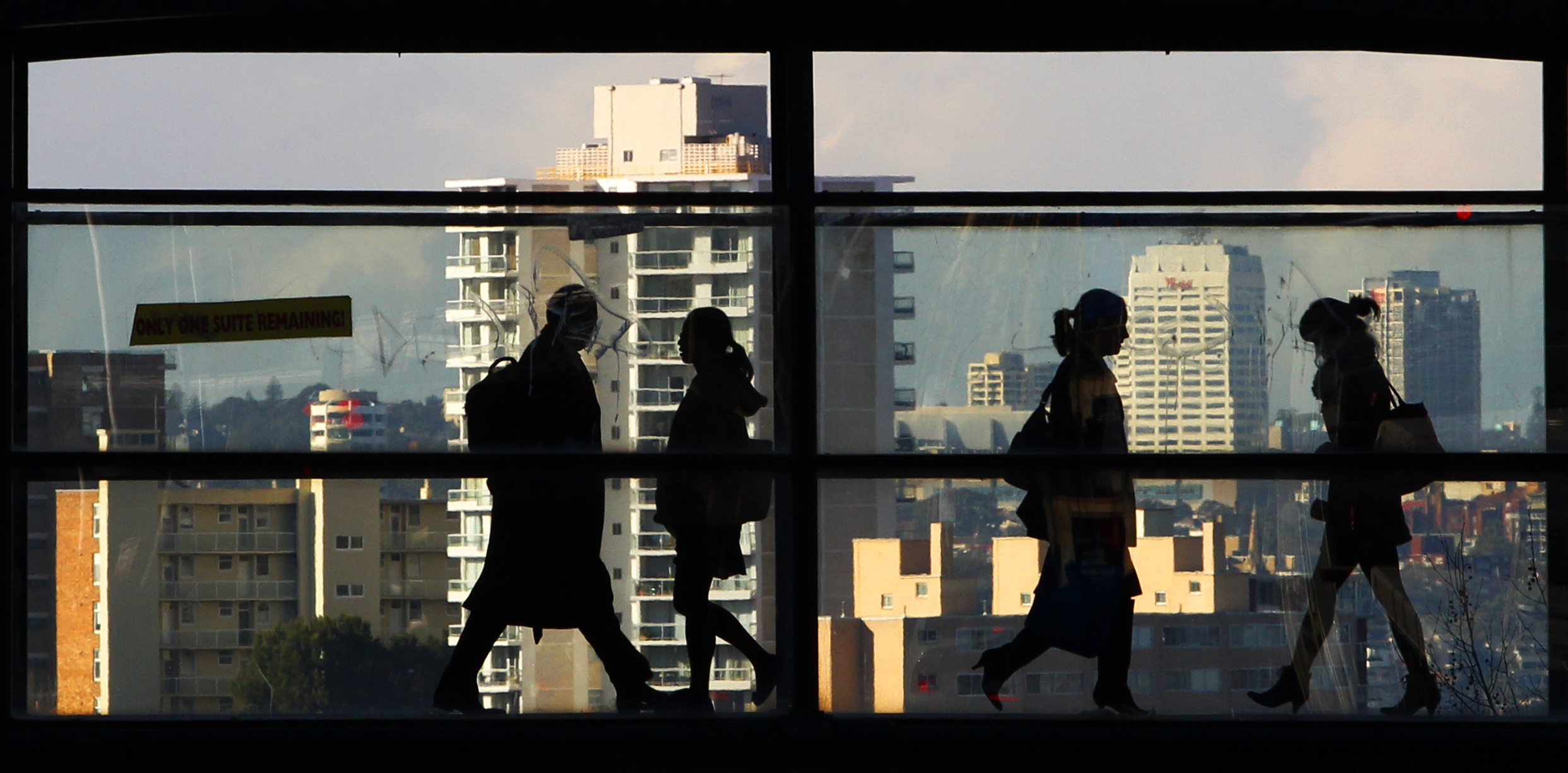 Peak-hour commuters walk across a glass walled bridge between office buildings in Sydney