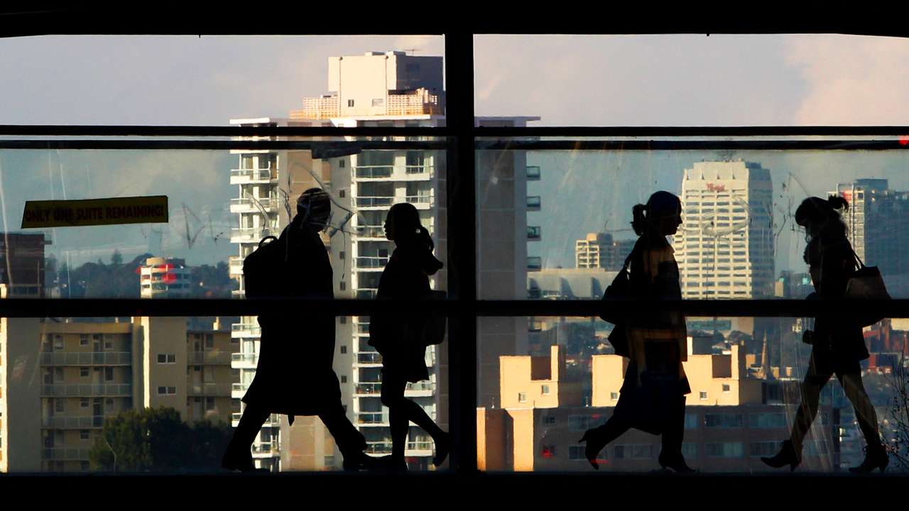 Peak-hour commuters walk across a glass walled bridge between office buildings in Sydney