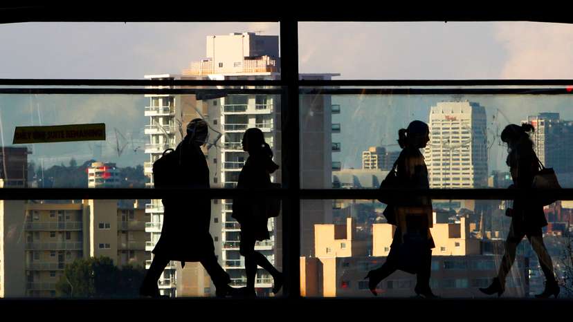 Peak-hour commuters walk across a glass walled bridge between office buildings in Sydney