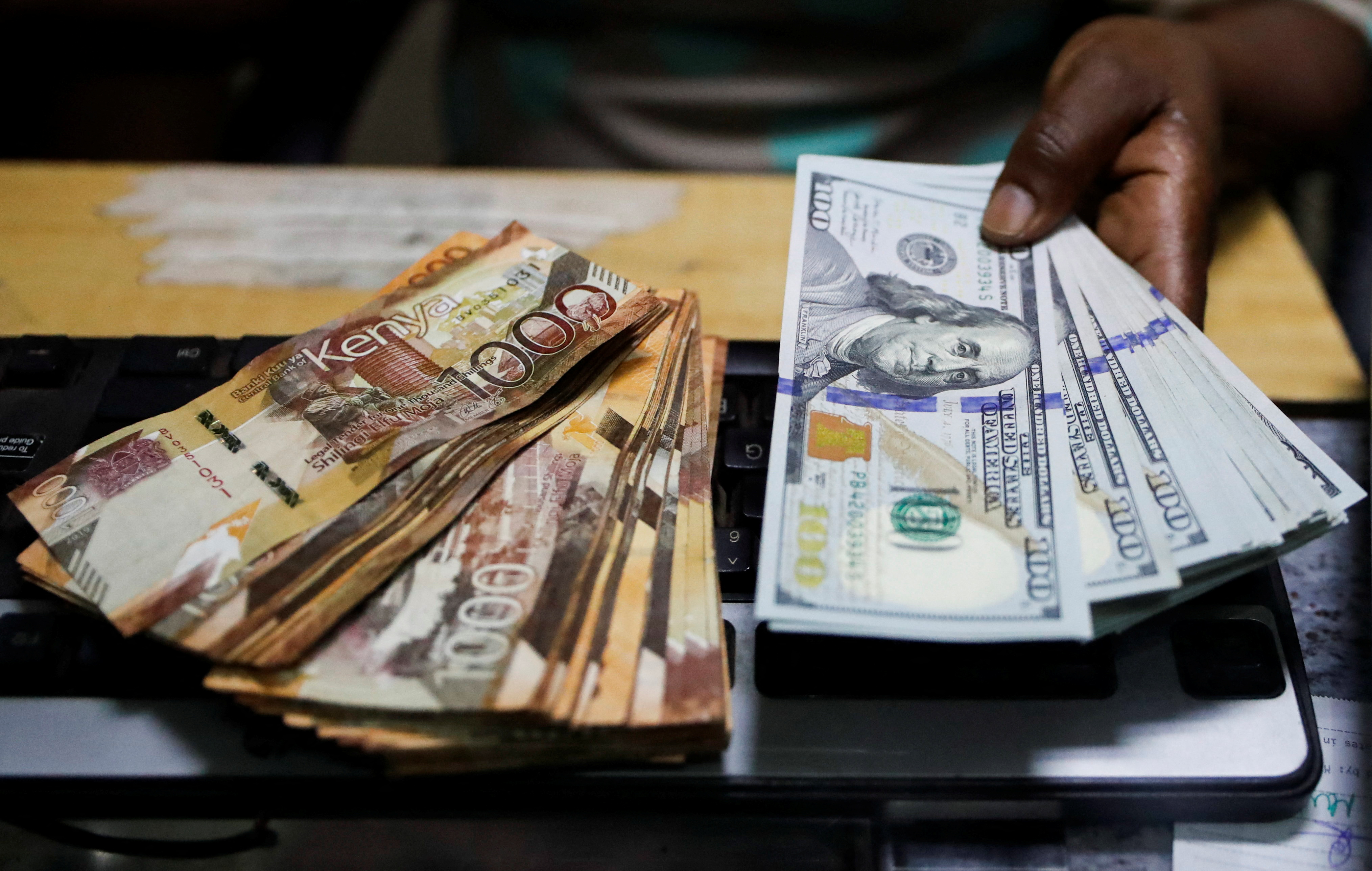 Teller handles U.S. dollar banknotes and Kenya shilling banknotes inside the cashier's booth at a forex exchange bureau in downtown Nairobi