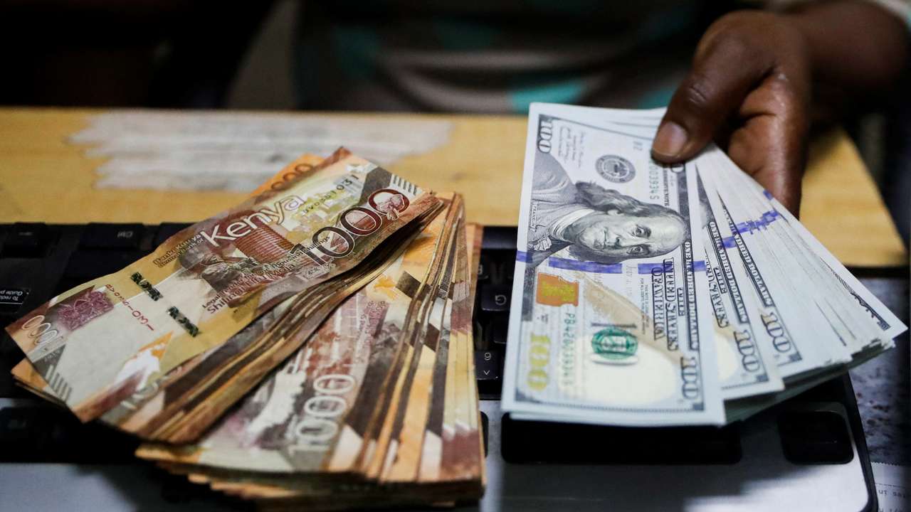 Teller handles U.S. dollar banknotes and Kenya shilling banknotes inside the cashier's booth at a forex exchange bureau in downtown Nairobi