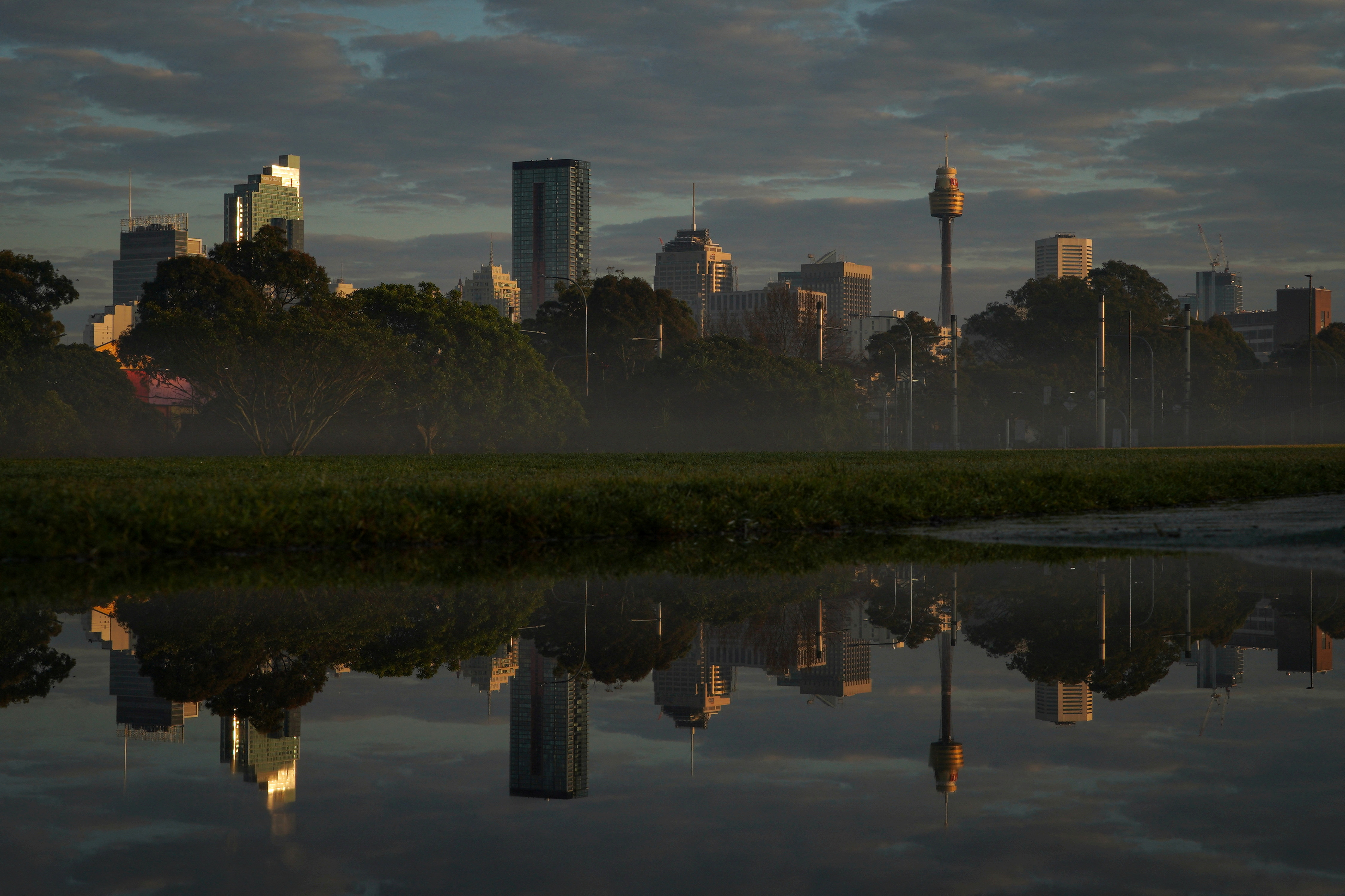 The city skyline is reflected in a puddle at sunrise following rainy weather in Sydney