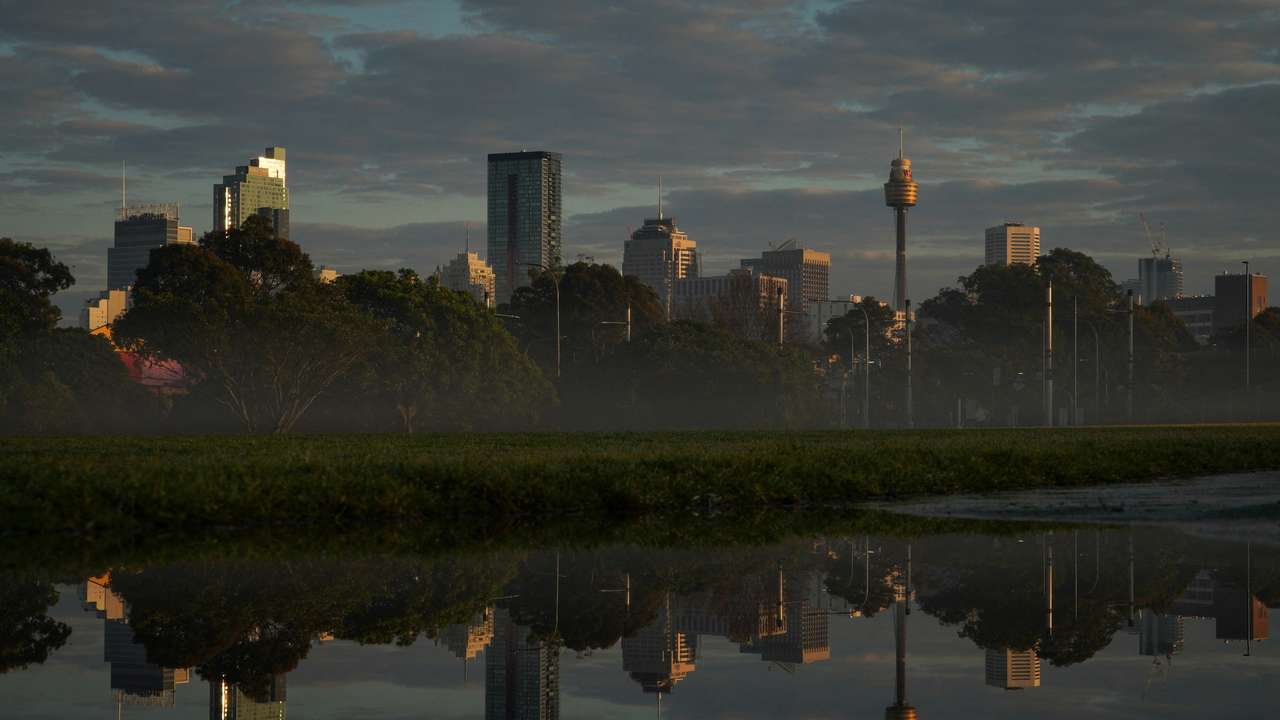 The city skyline is reflected in a puddle at sunrise following rainy weather in Sydney