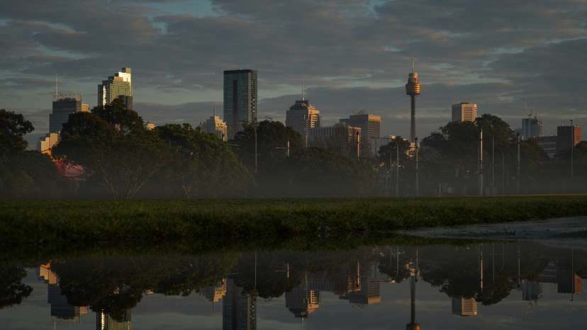 The city skyline is reflected in a puddle at sunrise following rainy weather in Sydney
