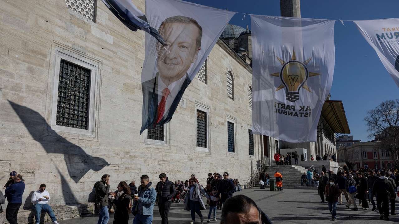 FILE PHOTO: People walk under election posters for Turkey's President Tayyip Erdogan and his ruling AK Party flags in Istanbul