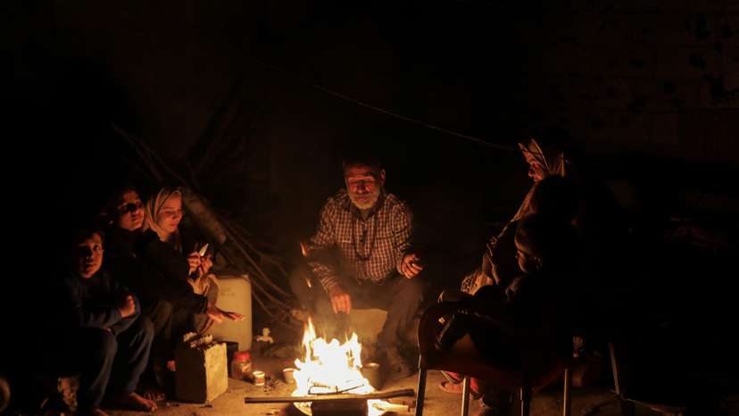 Palestinians sit next to a fire, amid a ceasefire between Israel and Hamas, in Jabalia