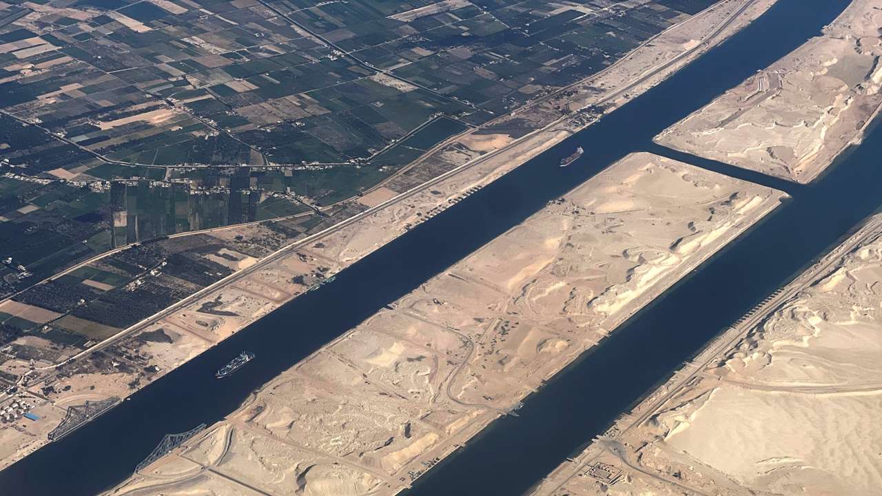 Ships are seen from a plane window, passing through the Suez Canal