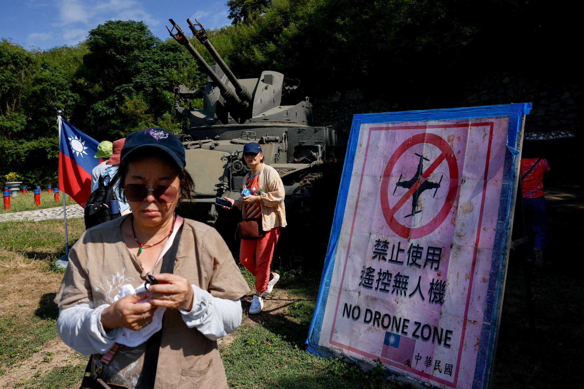 Tourists walk past a "No Drone Zone" sign next to a self-propelled anti-aircraft gun on display facing China's Xiamen, on Dadan Island