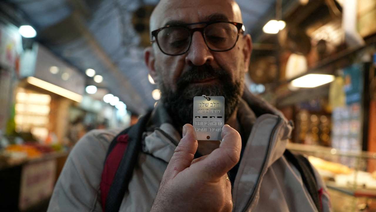 A man holds up a military-style dog tag calling for the return of Israeli hostages who have been held in the Gaza Strip since they were seized by Hamas gunmen on October 7, at Mahane Yehuda market in Jerusalem