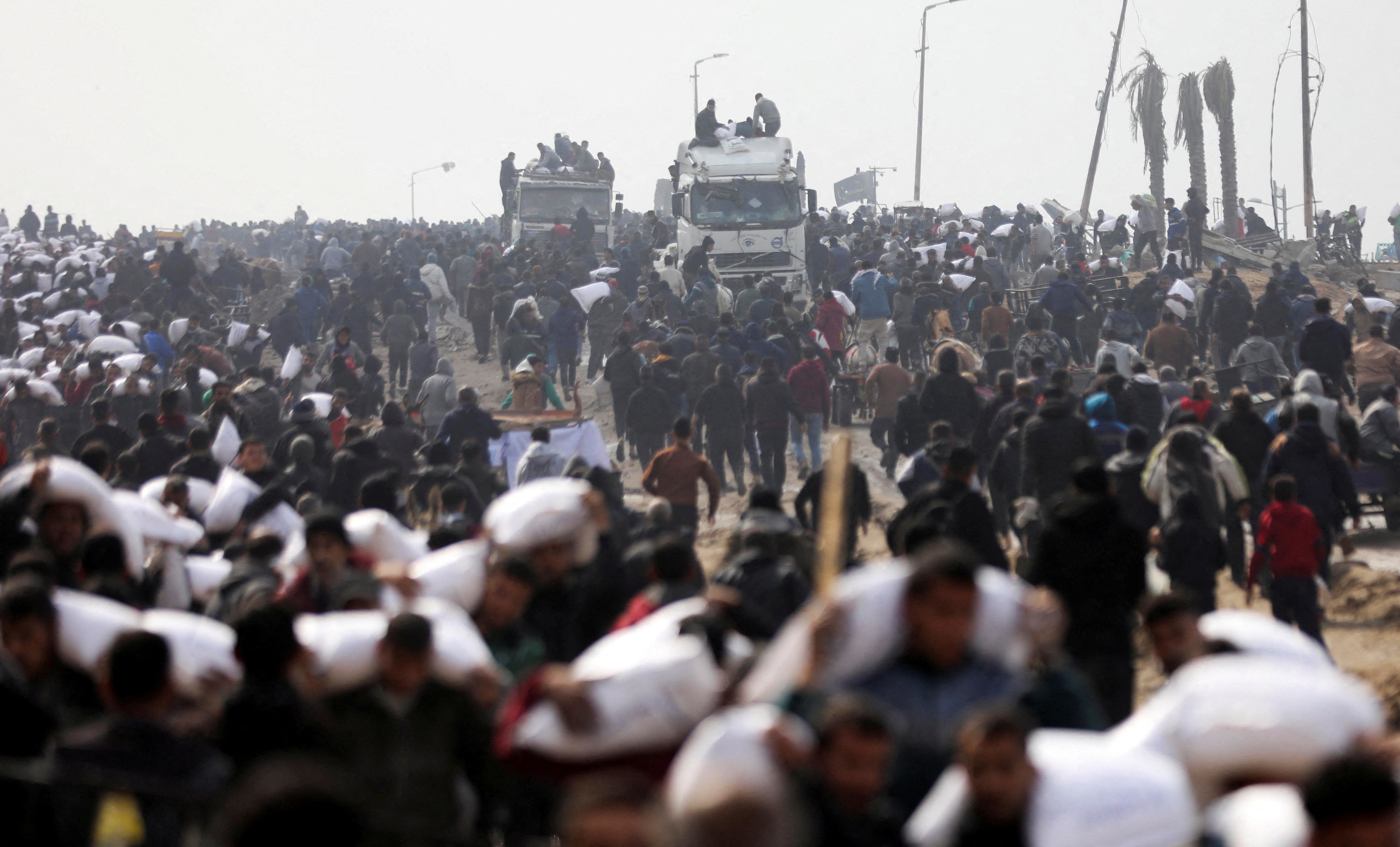 FILE PHOTO: Palestinians carry bags of flour they grabbed from an aid truck near an Israeli checkpoint in Gaza City