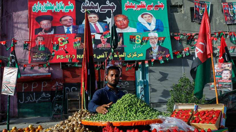 Fruit vendor waits for customers in front of a makeshift office with campaign posters of a political party, ahead of general elections, in Karachi