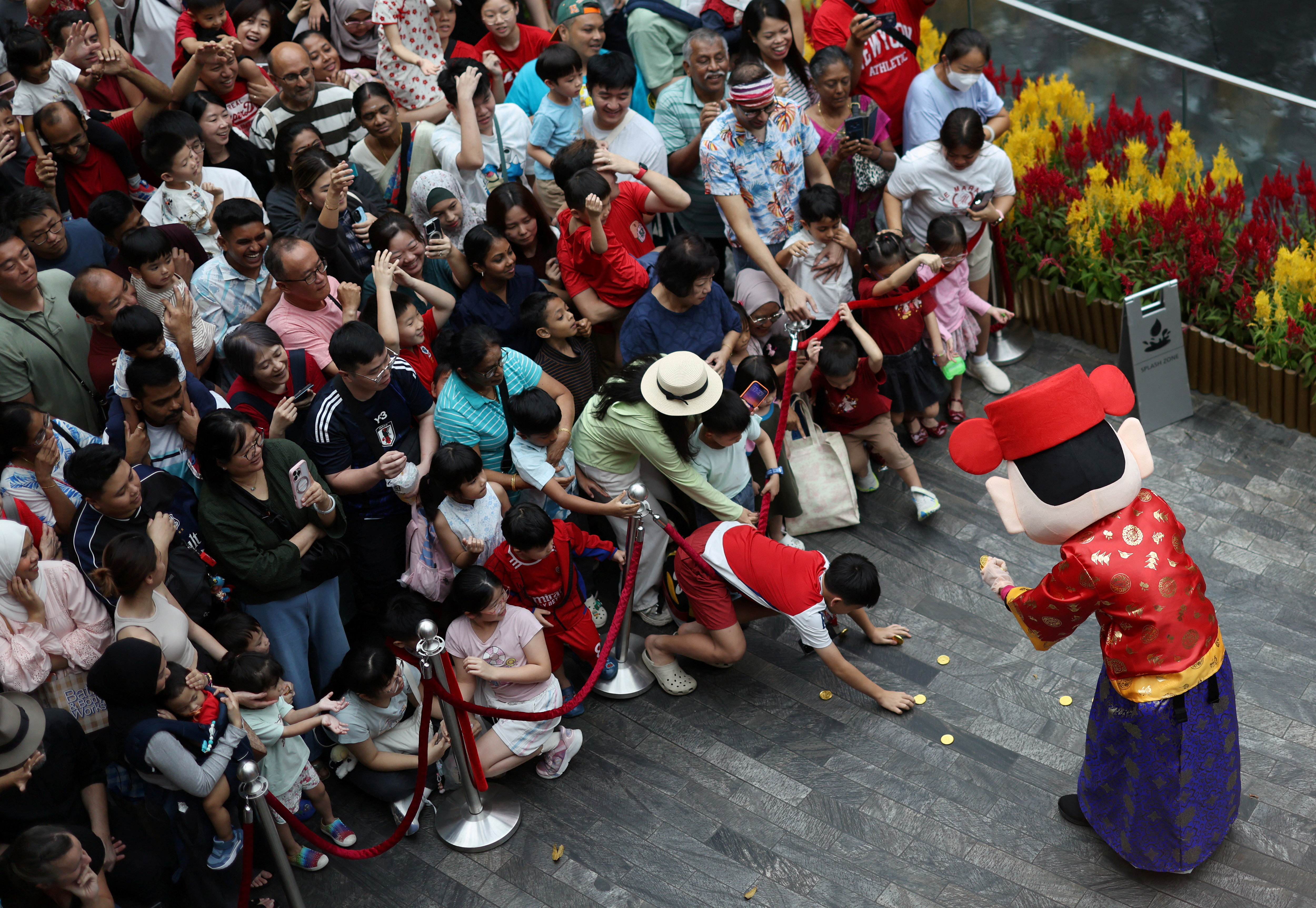 People catch coins from a God of Fortune performer during a lion dance performance on the eve of the Lunar New Year at Jewel Changi Airport in Singapore
