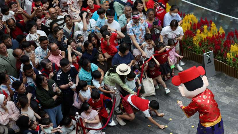 People catch coins from a God of Fortune performer during a lion dance performance on the eve of the Lunar New Year at Jewel Changi Airport in Singapore