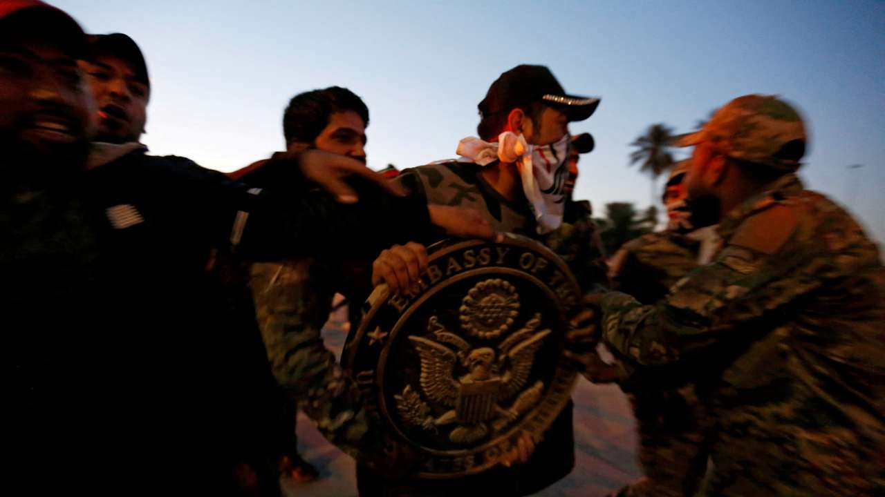 FILE PHOTO: Protesters and militia fighters carry the logo of the U.S. Embassy, during a protest to condemn air strikes on bases belonging to Hashd al-Shaabi (paramilitary forces), in Baghdad