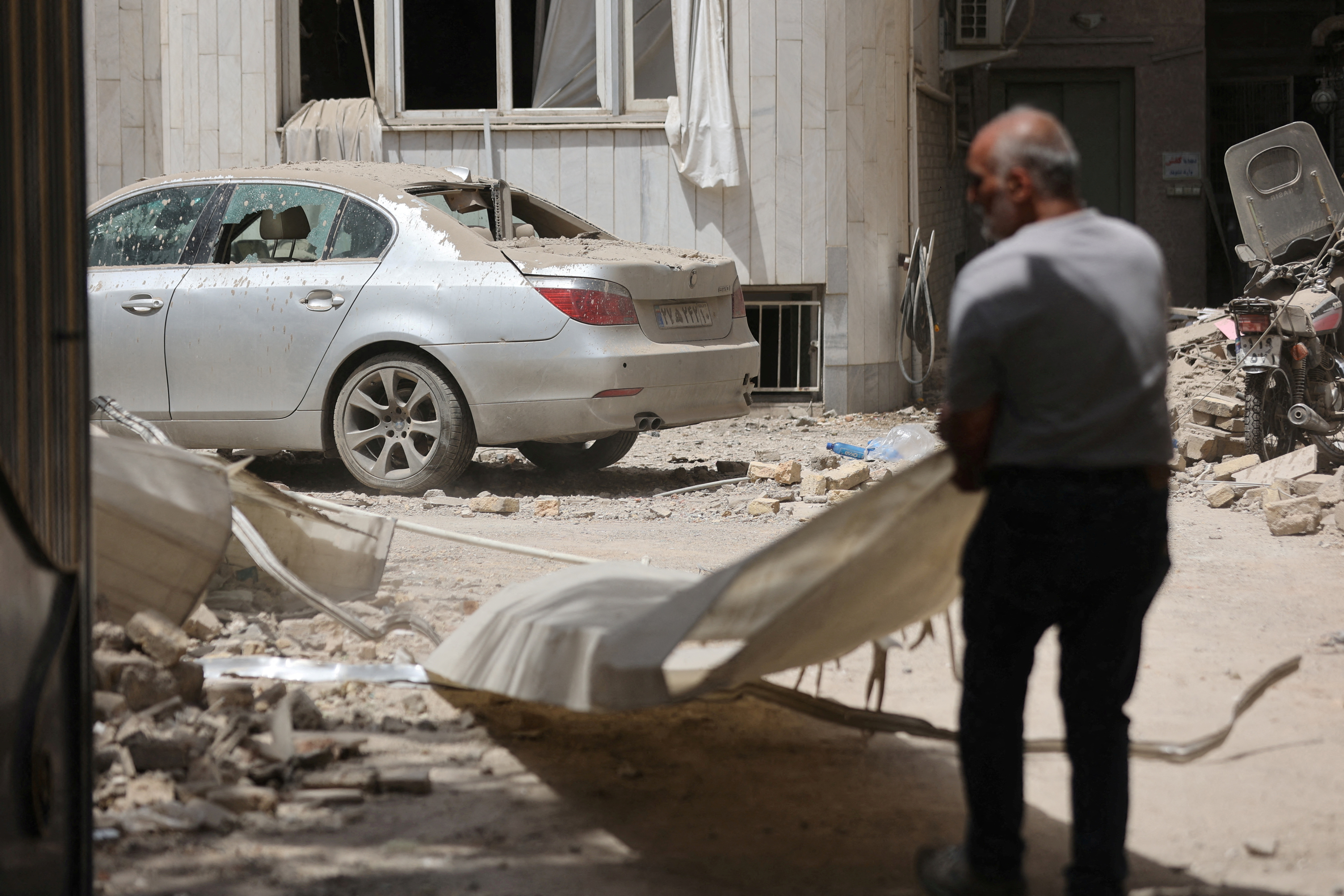 FILE PHOTO: A man stands near a damaged car at an impacted residential site, following an Israeli strike on Monday, after the ceasefire between Israel and Iran, in Tehran
