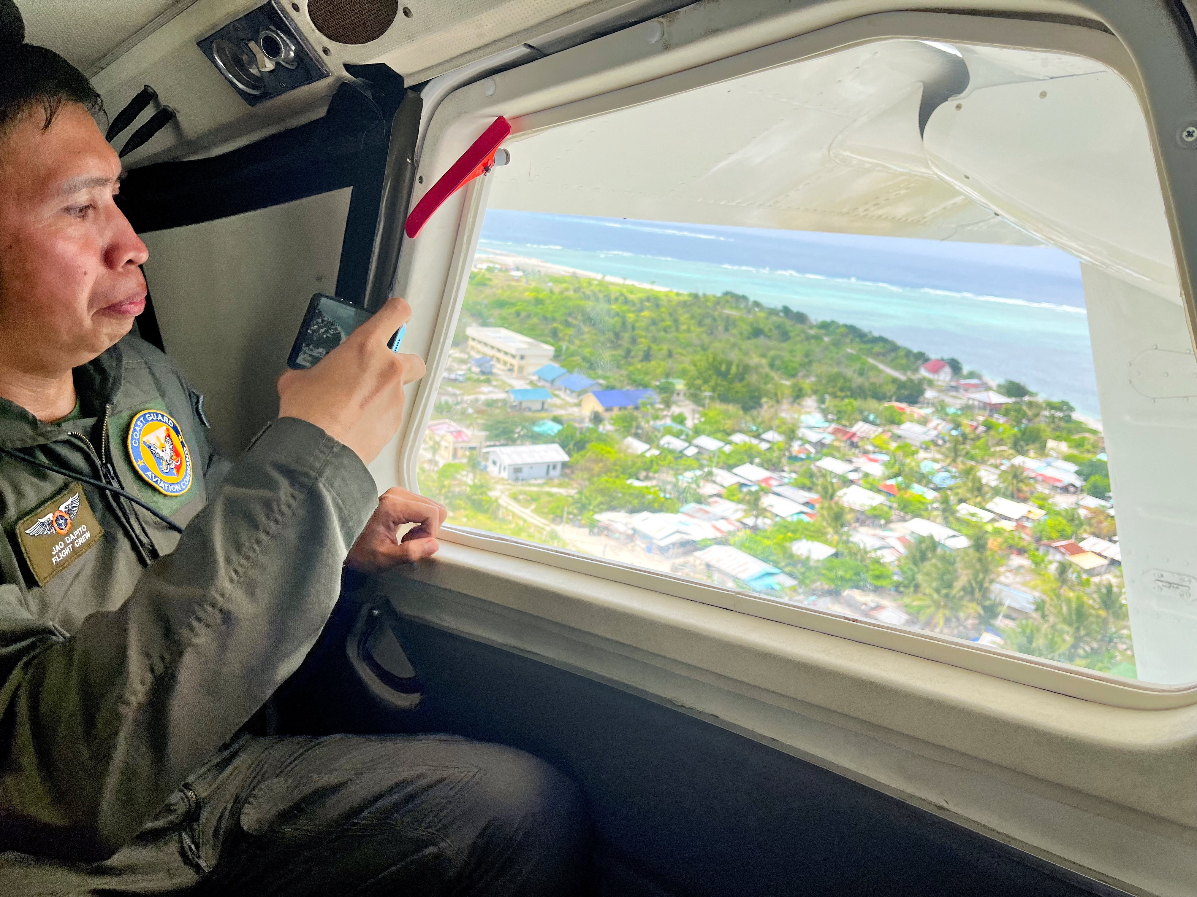 A Philippine Coast Guard member uses his phone to record the view of Philippine-occupied Thitu Island while onboard a plane in the disputed South China Sea