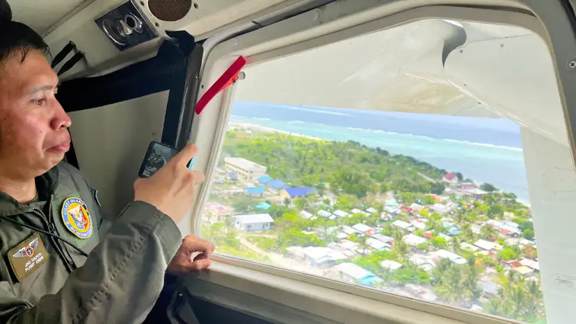 A Philippine Coast Guard member uses his phone to record the view of Philippine-occupied Thitu Island while onboard a plane in the disputed South China Sea