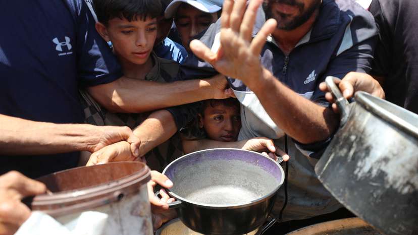 Palestinians wait to receive food cooked by a charity kitchen, in Gaza City