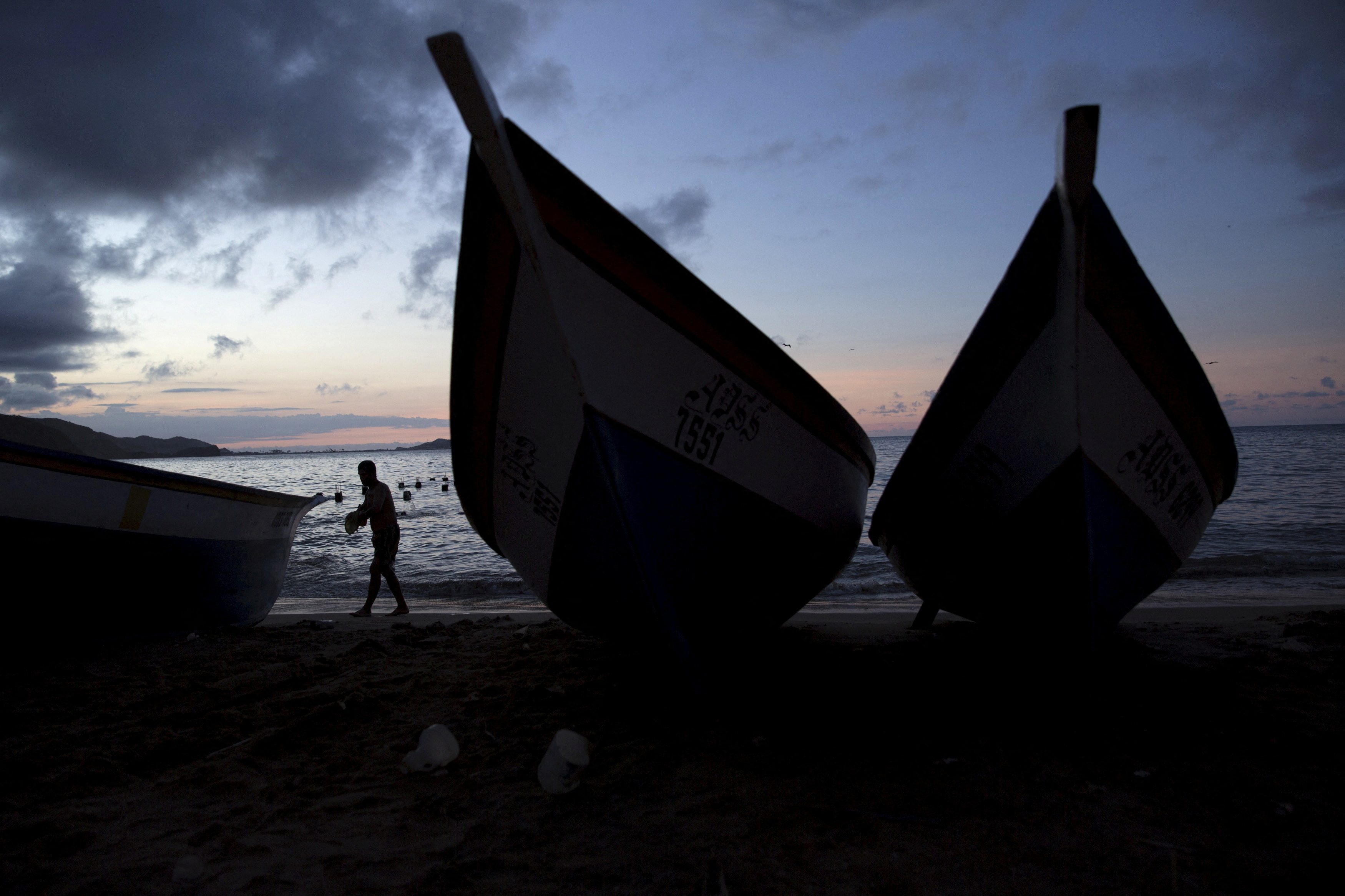 FILE PHOTO: A man walks past wooden boats in the bay of Rio Caribe a town near caribbean islands, in the eastern state of Sucre, Venezuela