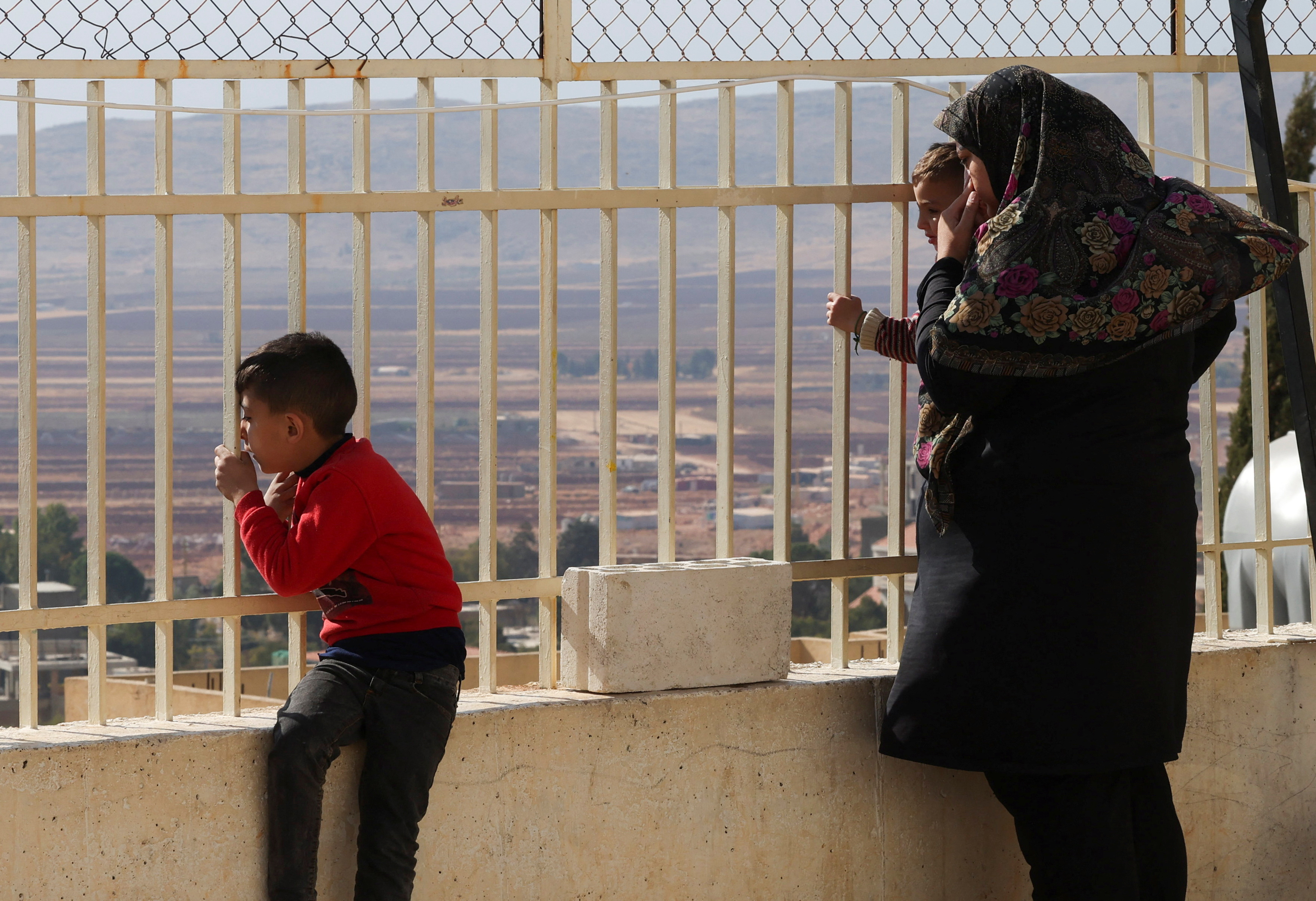 Displaced people look out from behind a fence at a school turned into a shelter in Deir al-Ahmar