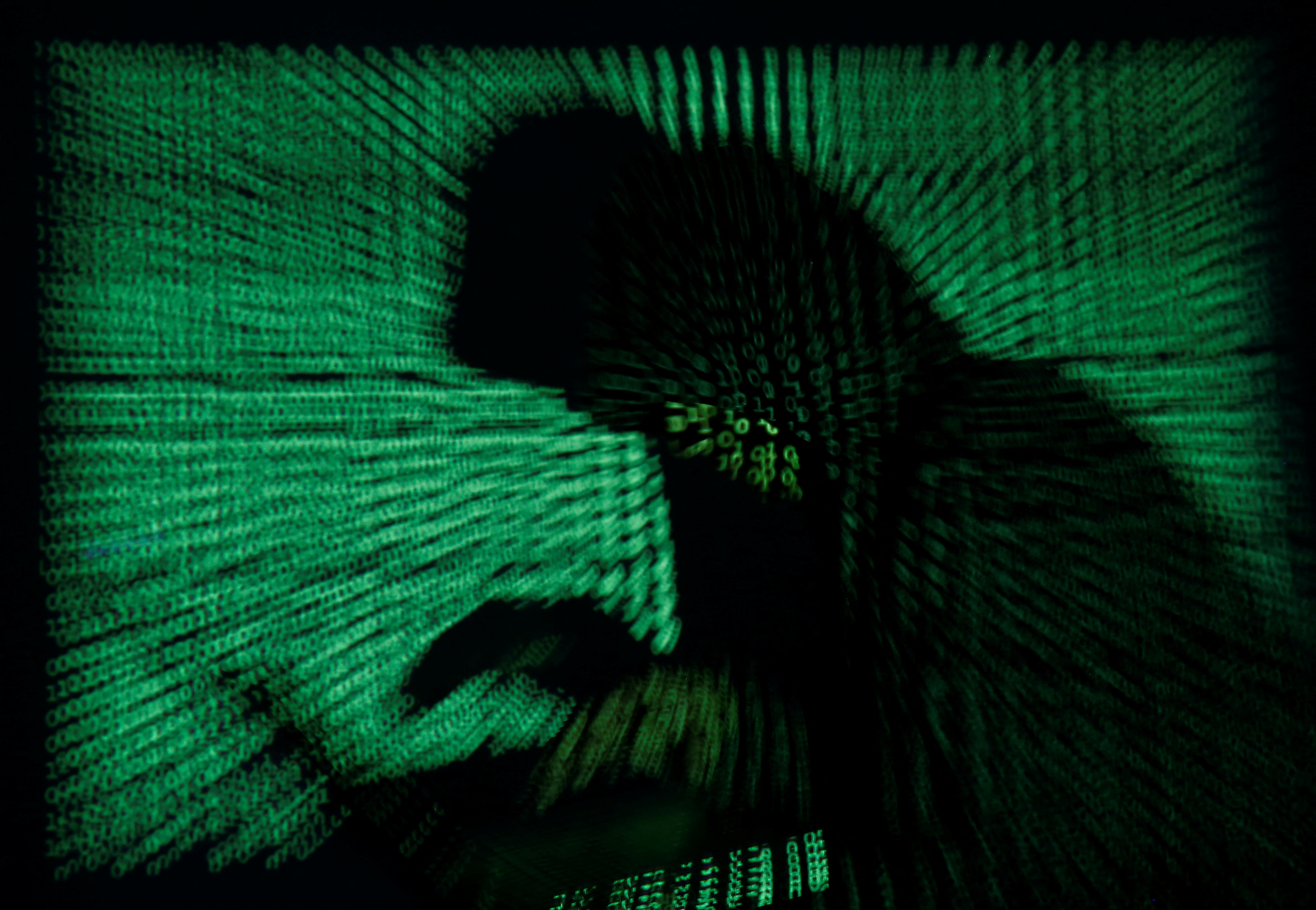 Hooded an holds laptop computer as cyber code is projected on him in this illustration picture