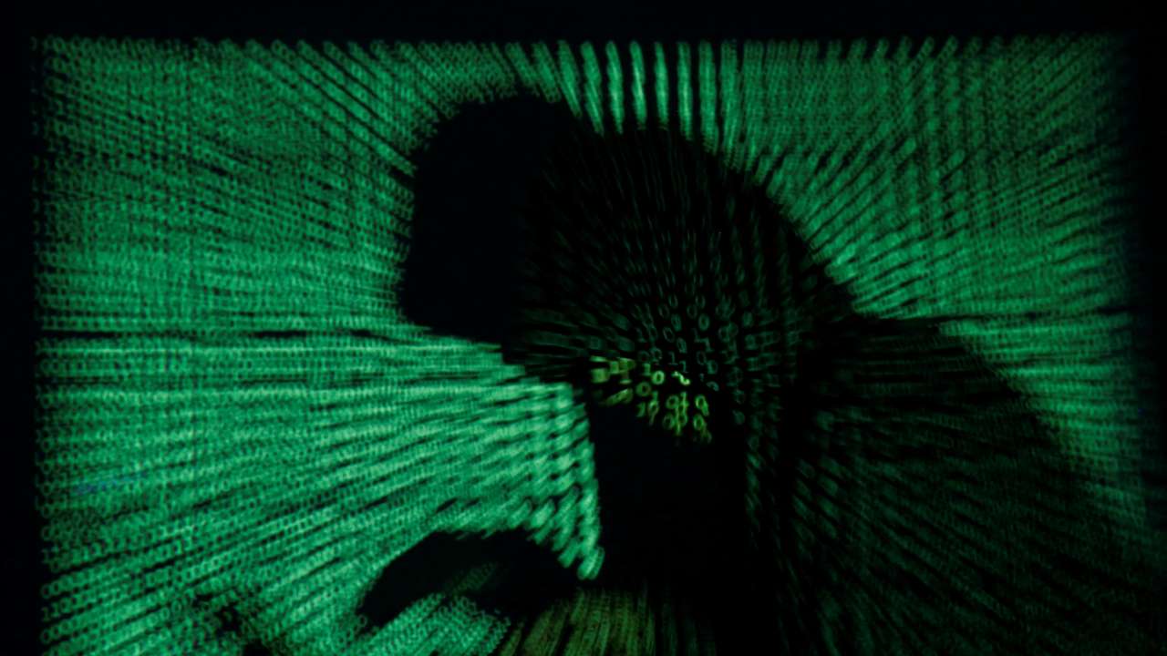 Hooded an holds laptop computer as cyber code is projected on him in this illustration picture