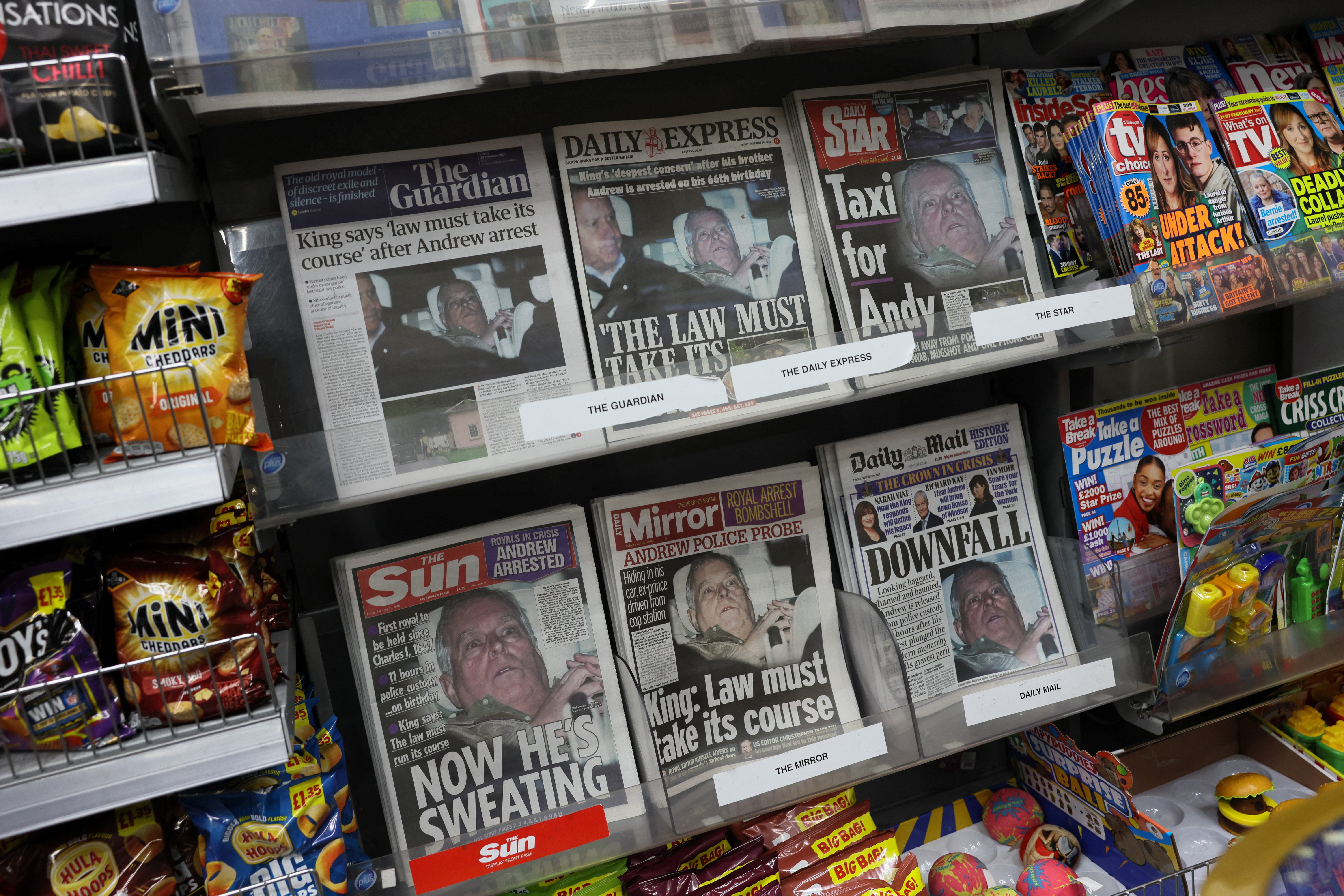 British newspapers, featuring coverage of the arrest of Andrew Mountbatten-Windsor, younger brother of Britain's King Charles, on suspicion of misconduct in public office, sit on display in a newsagent in London
