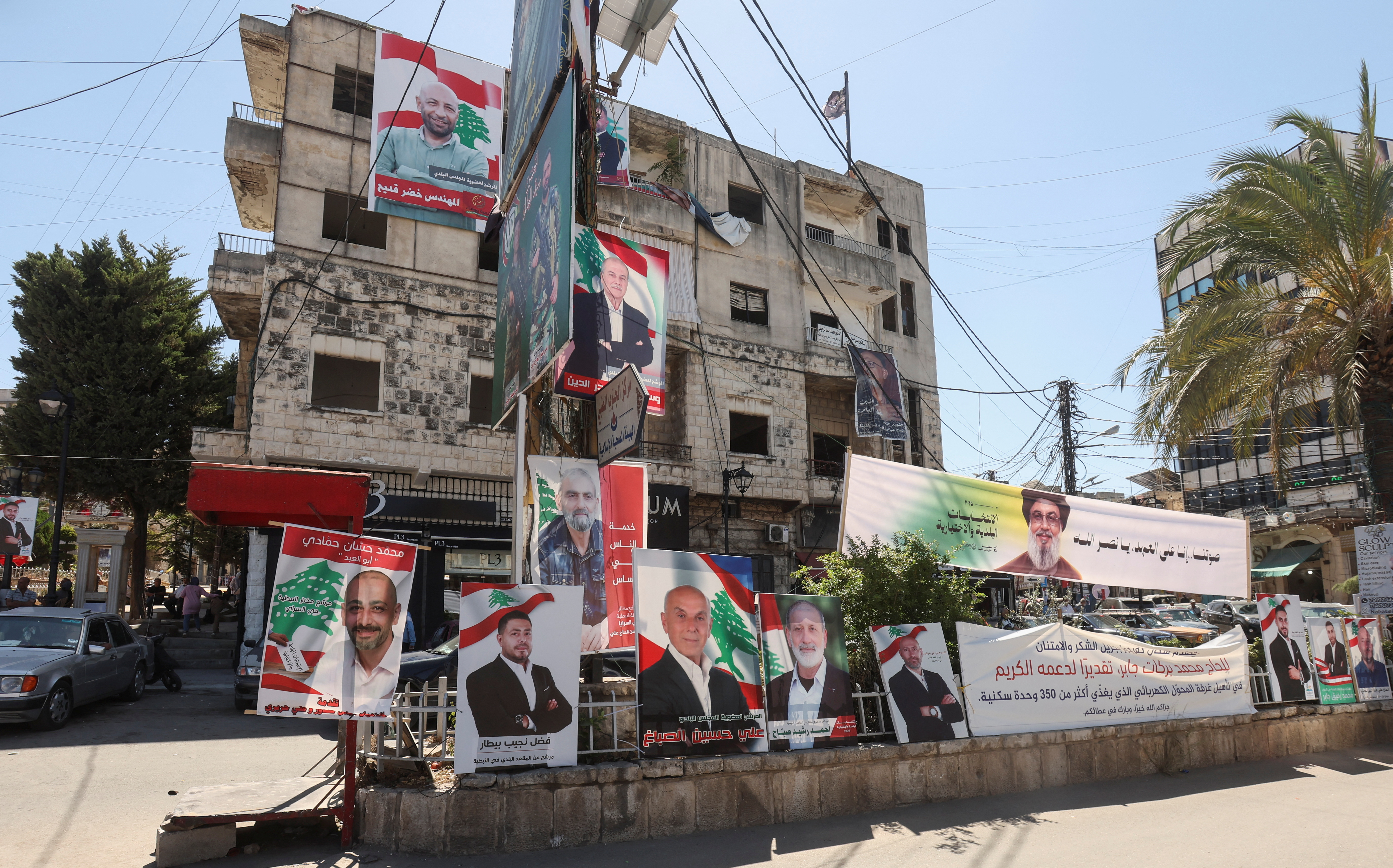 A banner depicting late Hezbollah leader Hassan Nasrallah and campaign poster of the candidates running for municipal elections, are placed along a street in Nabatieh