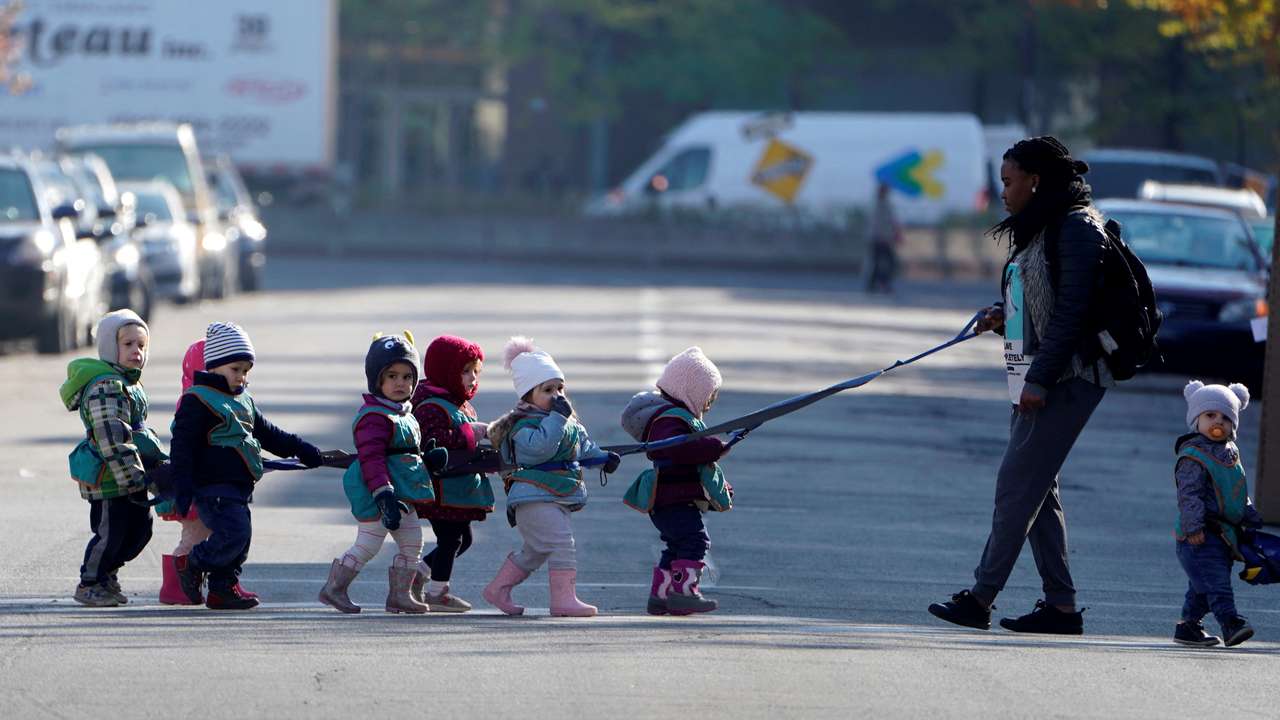 FILE PHOTO: A guardian escorts children on a tether while walking across a road in the Papineau area of Montreal