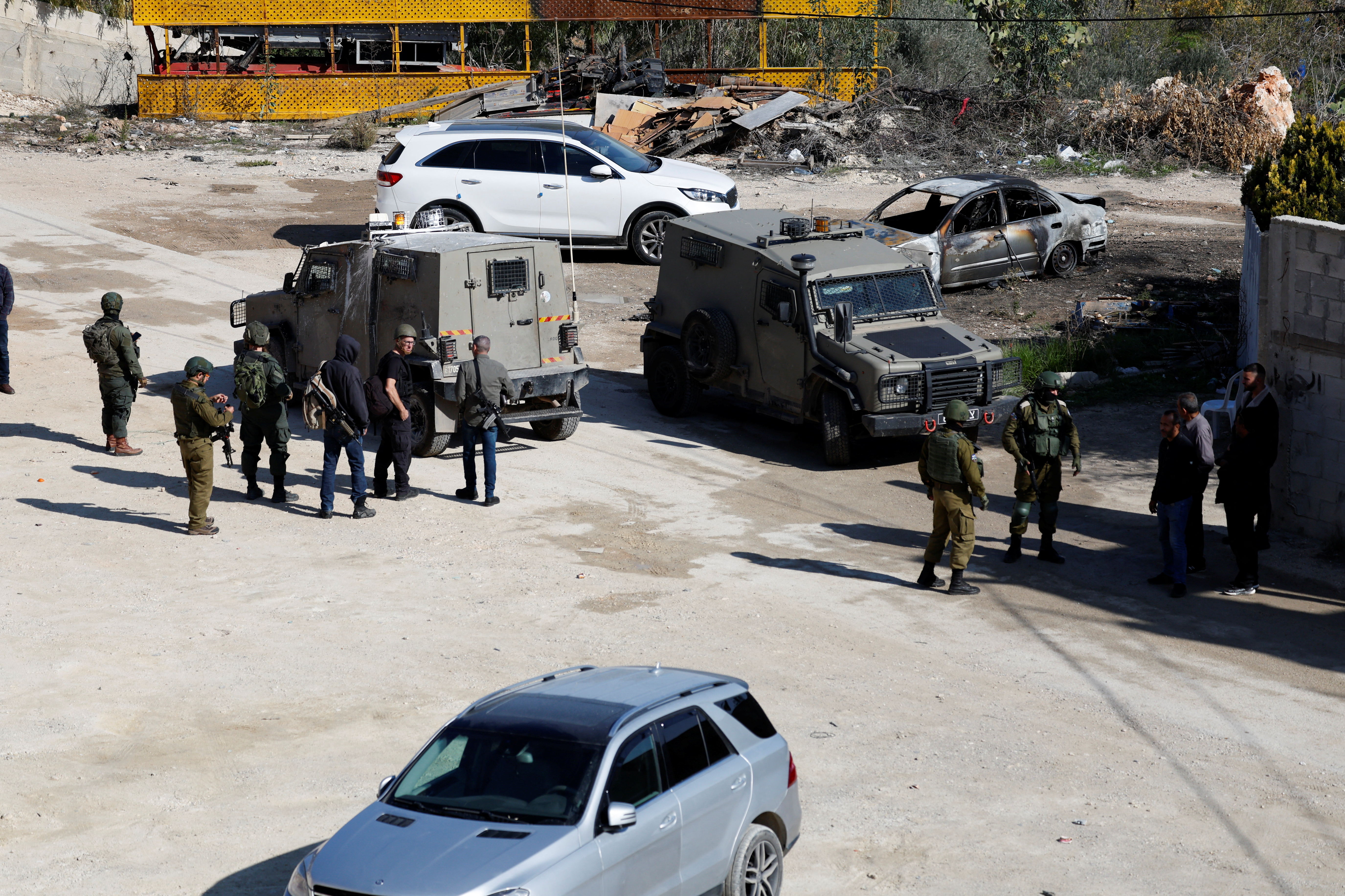 Israeli soldiers stand guard near a damaged car, after an Israeli settlers attack in Hawara near Nablus