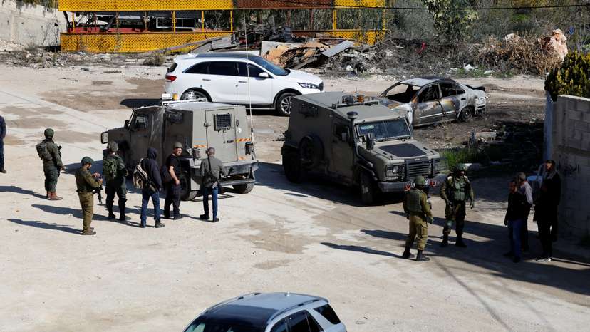 Israeli soldiers stand guard near a damaged car, after an Israeli settlers attack in Hawara near Nablus