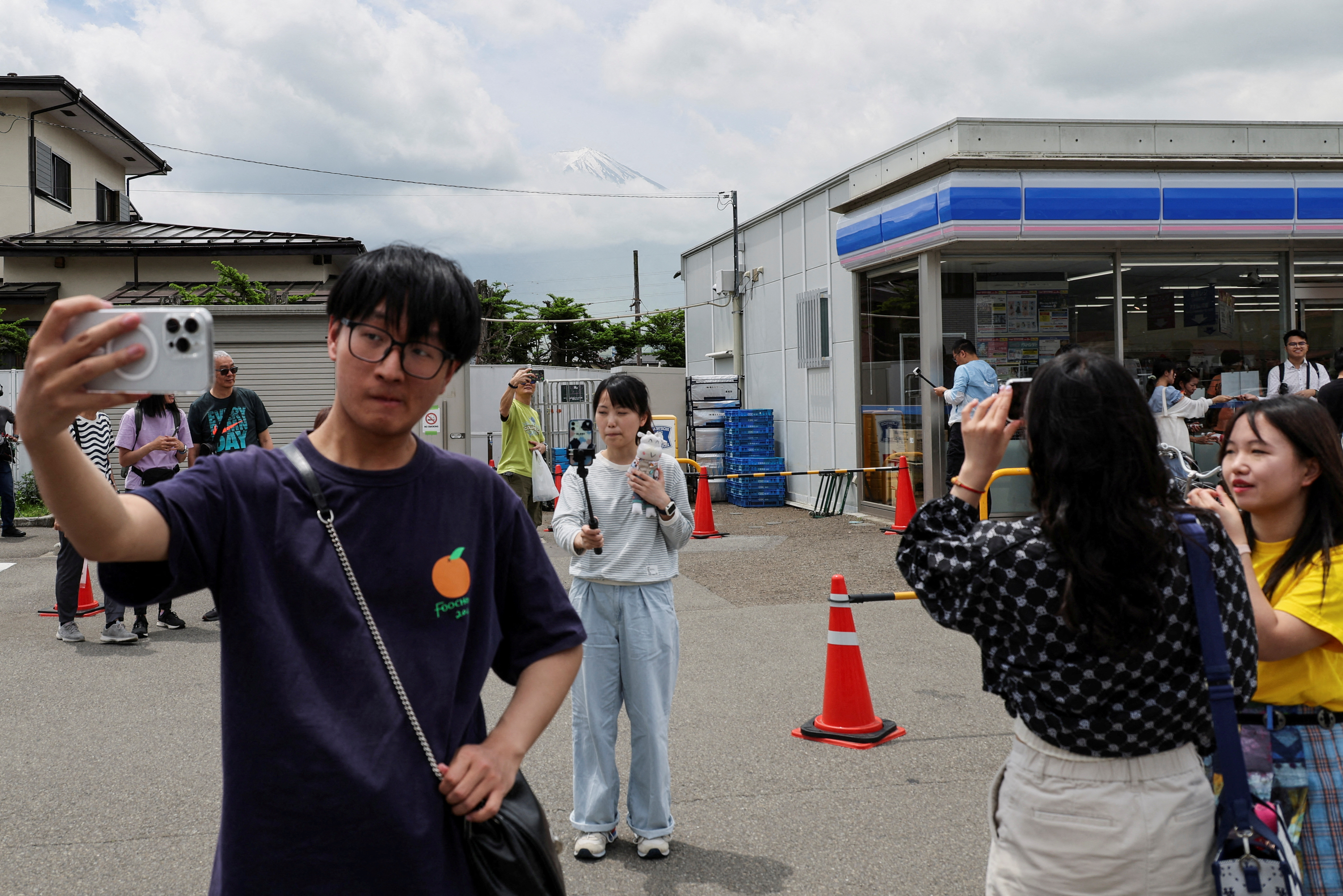 Tourists take photos of Mount Fuji appearing over a convenience store in Fujikawaguchiko town