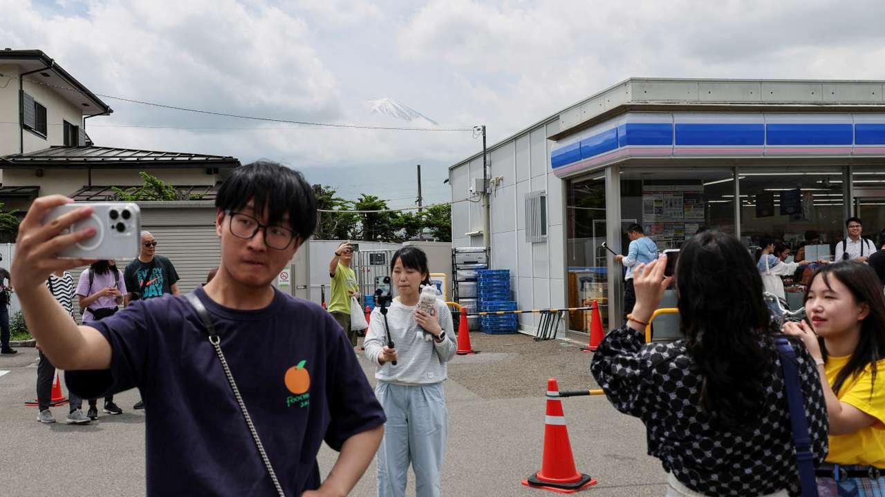 Tourists take photos of Mount Fuji appearing over a convenience store in Fujikawaguchiko town