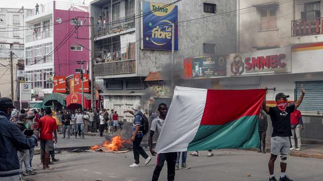 Supporters of opposition parties hold a national flag as they gesture in a sign of non-violence while walking towards the riot police officers during a protest ahead of the forthcoming first round of Madagascar's presidential election in Antananarivo