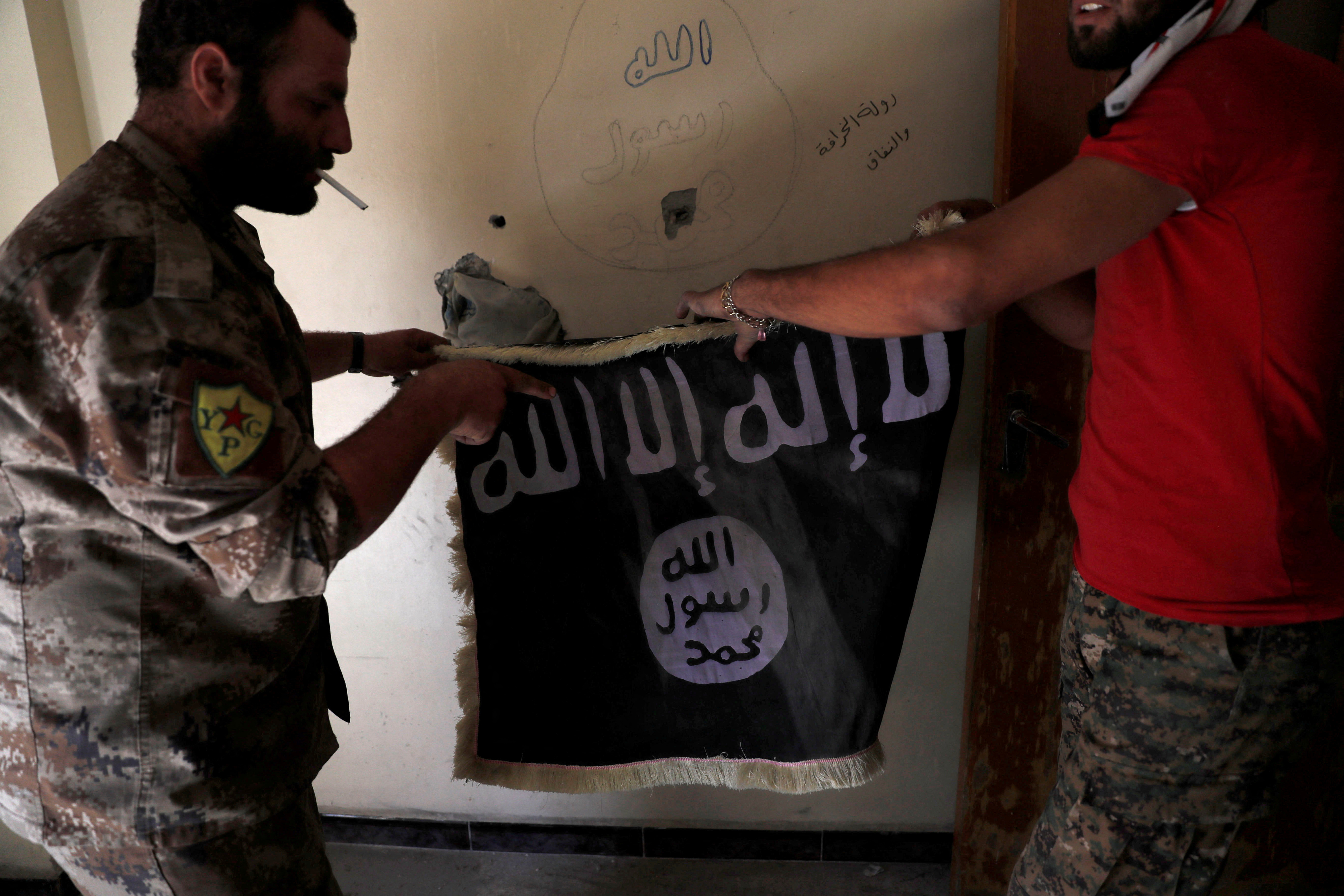 FILE PHOTO: Members of Syrian Democratic Forces hold a flag of the Islamic State militants recovered at a building next to the stadium in Raqqa