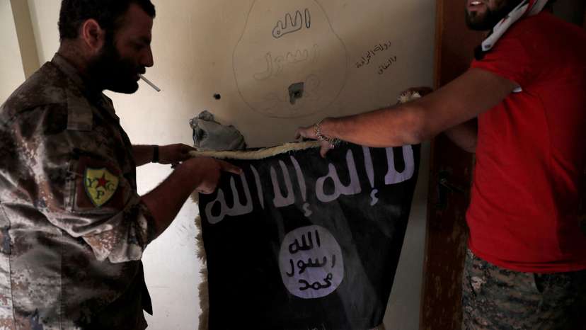 FILE PHOTO: Members of Syrian Democratic Forces hold a flag of the Islamic State militants recovered at a building next to the stadium in Raqqa