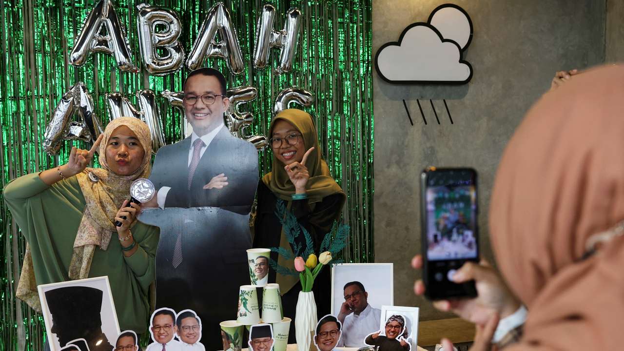 Women pose for a photograph with a cutout depicting Presidential candidate Anies Baswedan during the Humanies Cup Sleeve Event at the Kopi Nako cafe in Jakarta