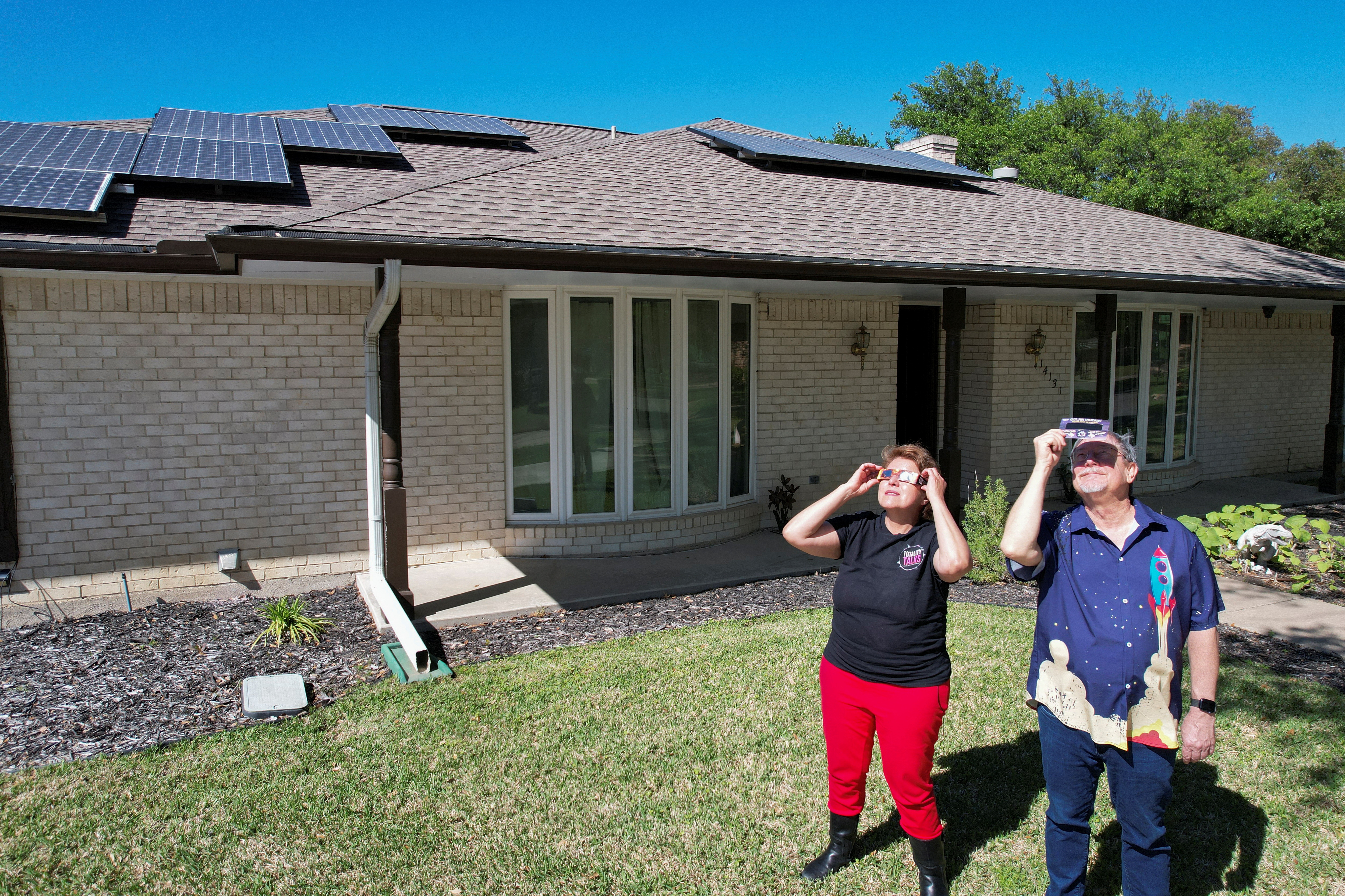 Eclipse chaser Leticia Ferrer and her husband Daniel Brookshier observe the sun through eclipse glasses, in front of their home in Dallas